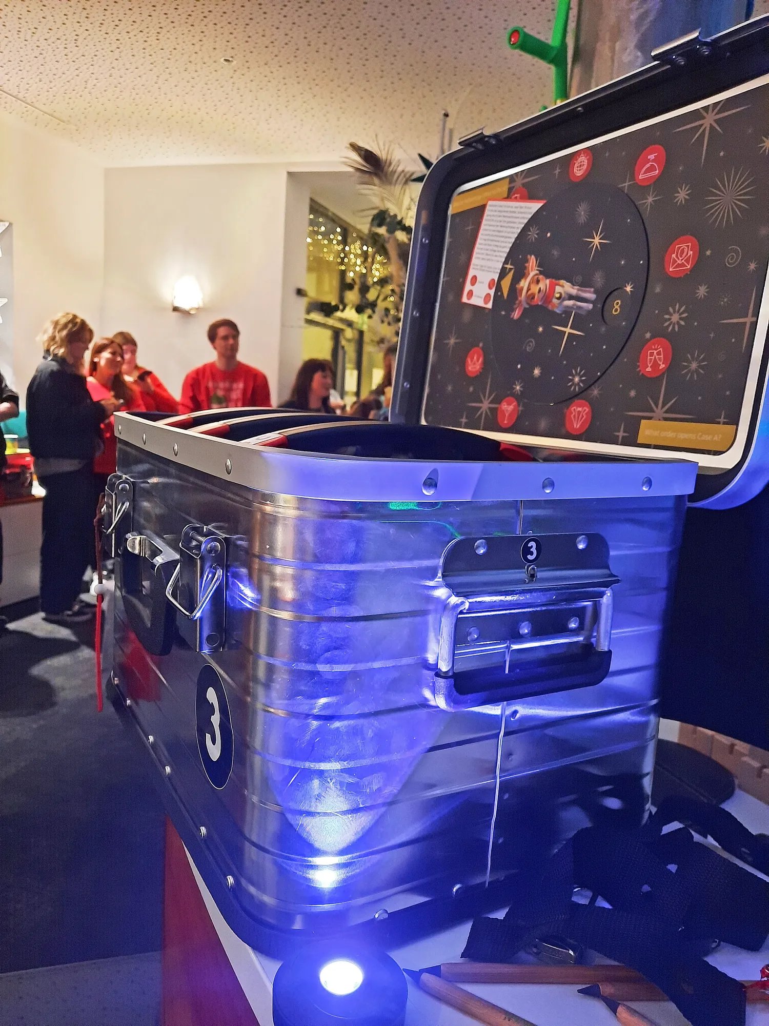 Geöffneter Rätselkoffer mit Rentier-Motiv und UV-Licht, im Hintergrund das Team